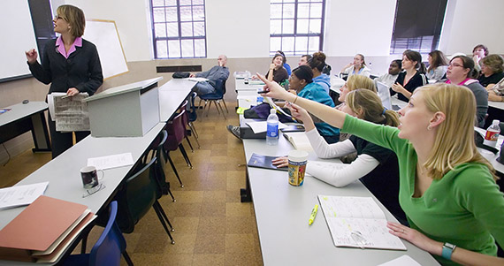 Photo of a faculty member leading a lecture with students behind desks asking questions.
